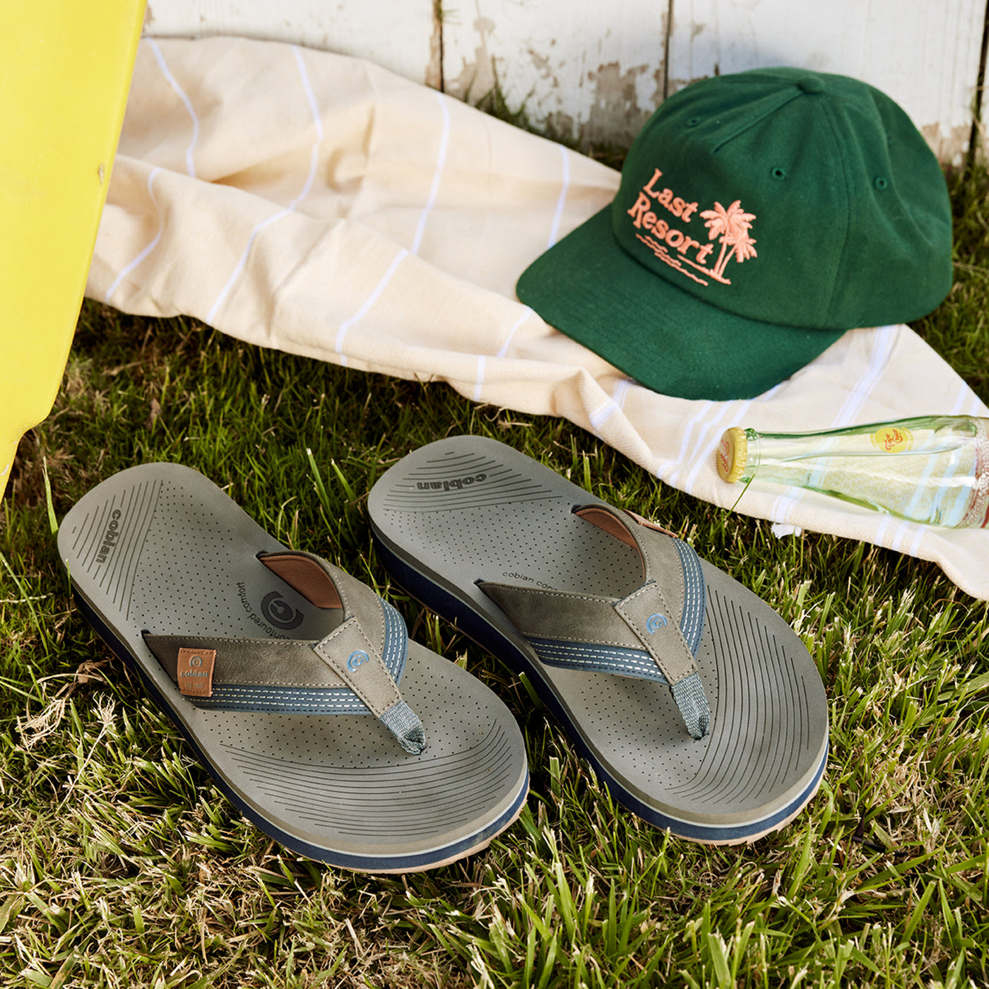 Close up of Cobian® Roca Rise™ Gray laying on grass next to a hat #color_gray