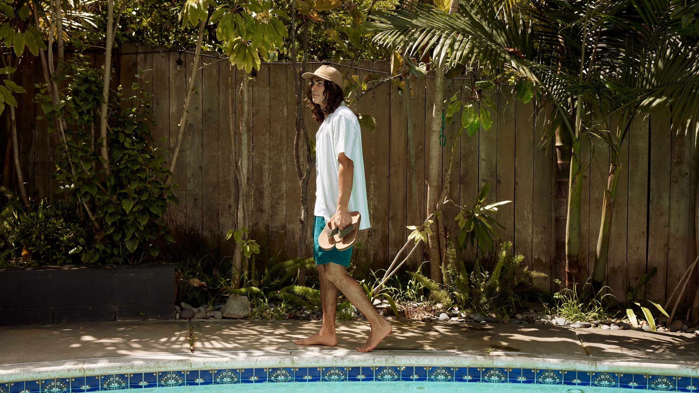 Model holding ARV 2 Sage while walking alongside a pool in a tropical backyard #color_sage