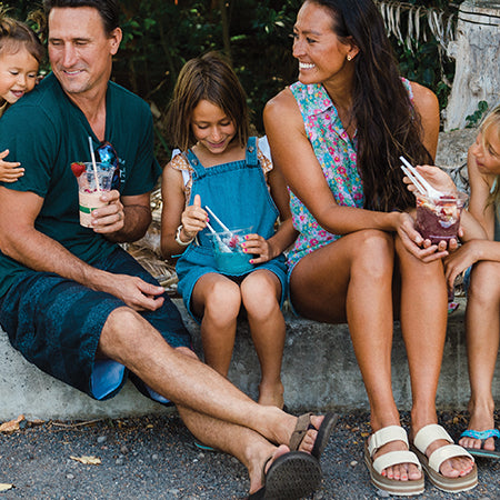 Father, mother, and two children sharing colorful smoothies outdoors.