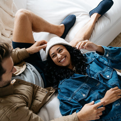 Model lounging with girlfriend on a white couch wearing the Cobian Dillon Slipper navy #color_navy
