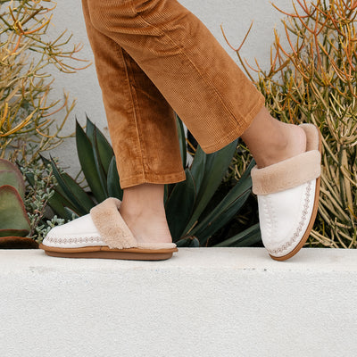 Model wearing the Cobian Colima Mule cream tip-toeing across a white ledge #color_cream