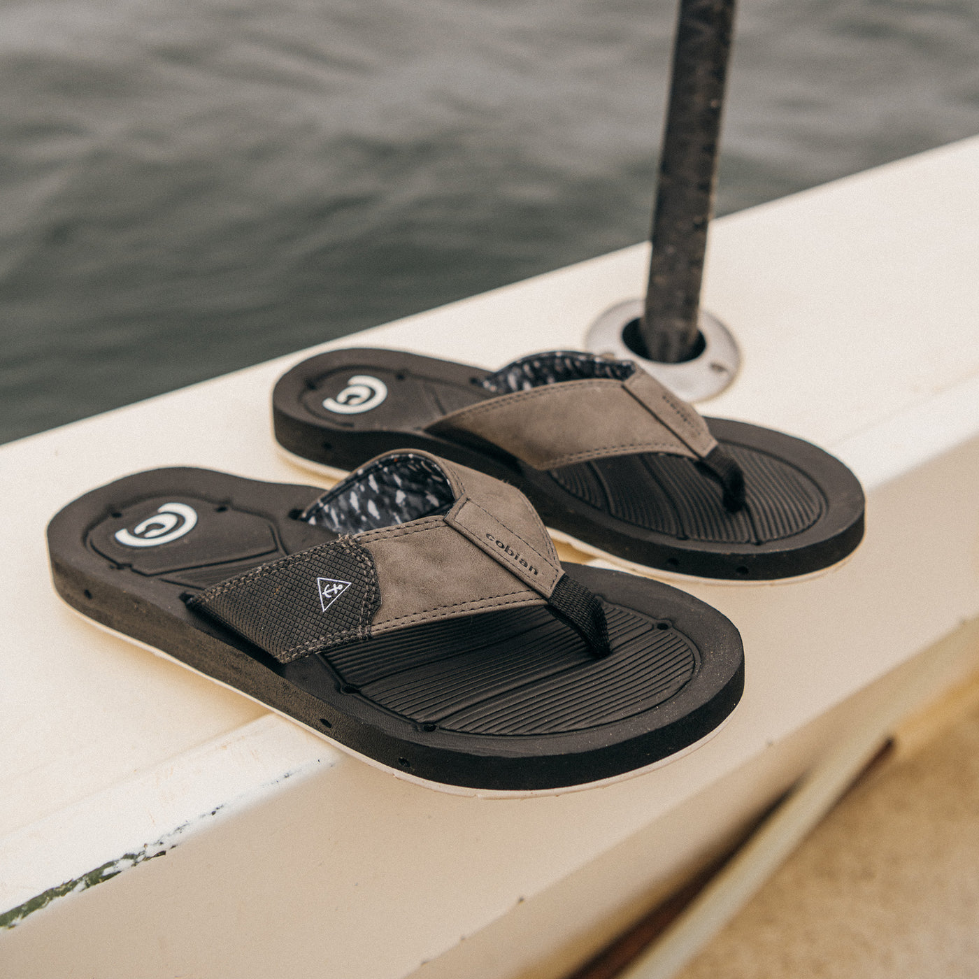 Cobian Draino 3 black sandals sitting on the rail of a fishing boat #color_black