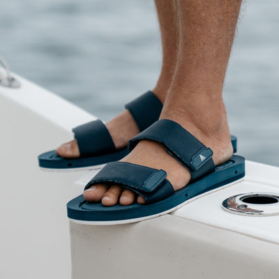 A closeup of Damien Hobgood wearing the Cobian Odyssey blue sandals on a boat deck #color_blue