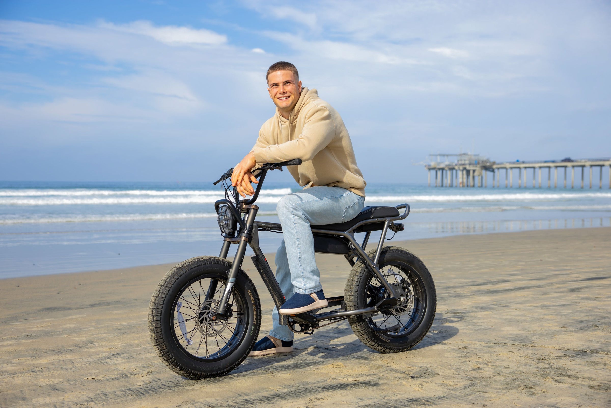 Man riding a electric bike on a beach with a pier in the background