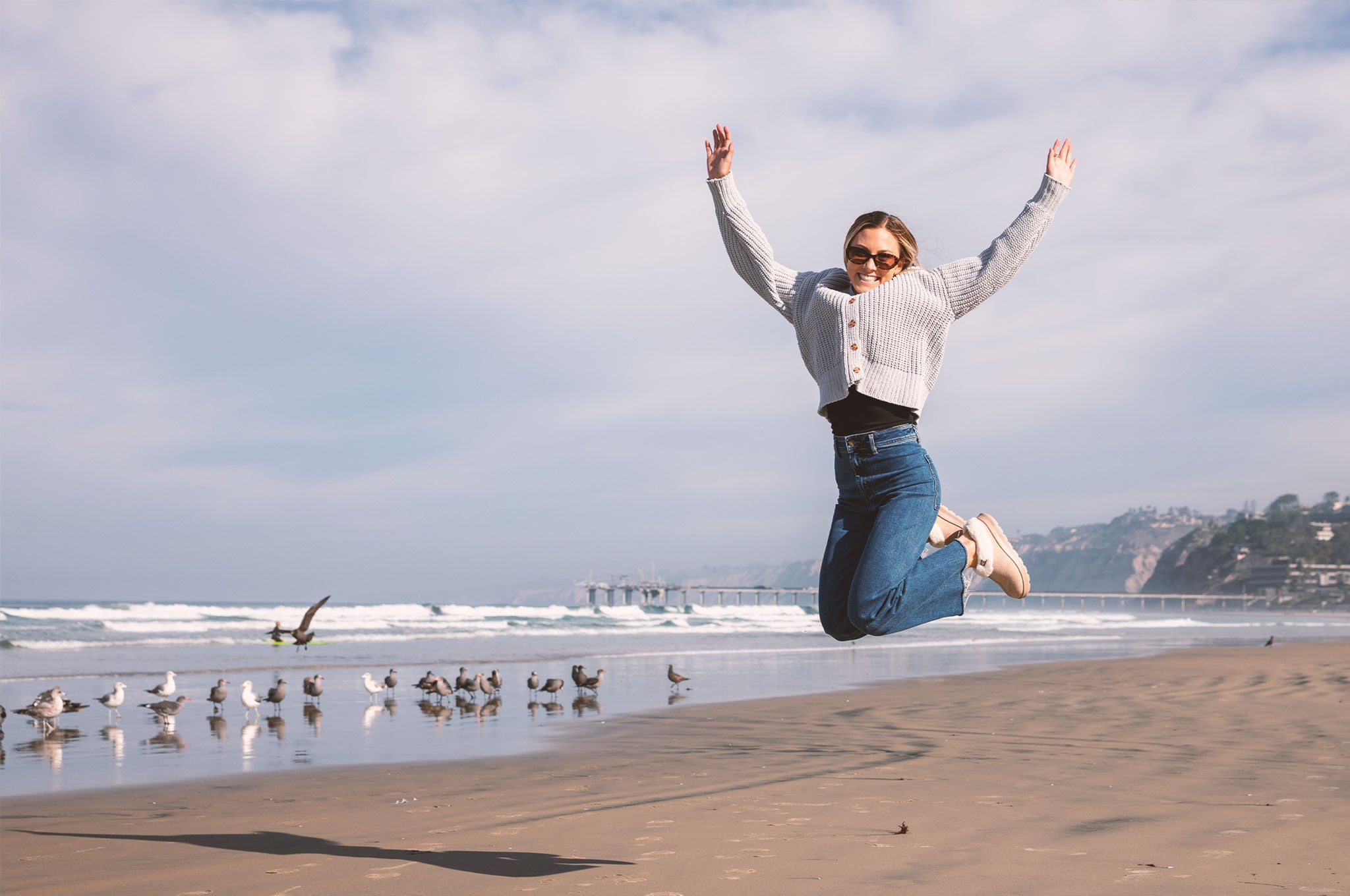 Woman jumping on a beach with seagulls and a scenic background