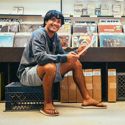 Model sitting on an upside-down carton in a record shop wearing Cobian® Ponto Rise™ Tan #color_tan