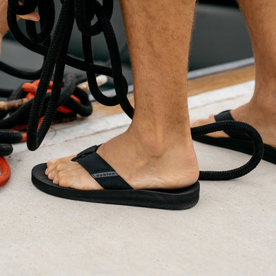 Closeup of a model wearing the Cobian ARV 2 black sandals on a boat dock #color_black