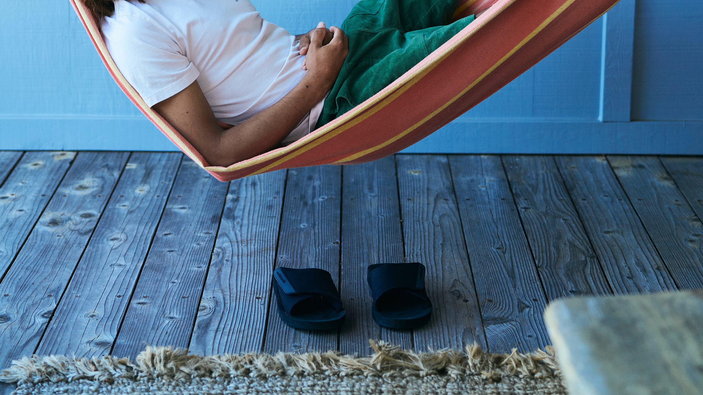 Model laying in hammock with ARV 2 Slide Black on wood floor below #color_black