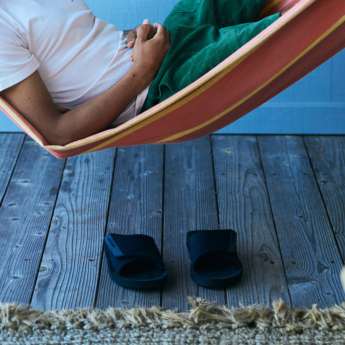 Model laying in hammock with ARV 2 Slide Black on wood floor below #color_black
